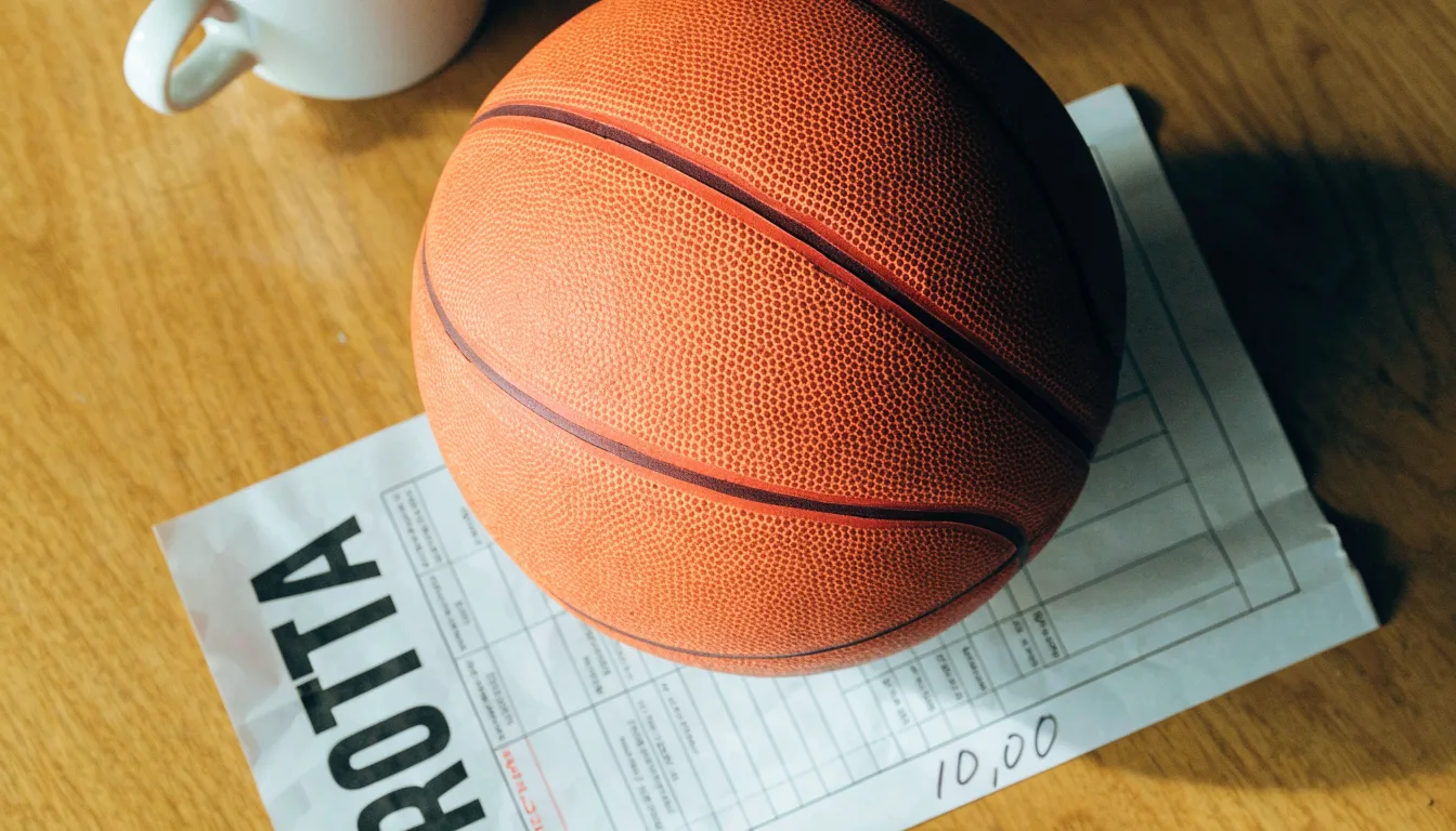 Uma bola de futebol pousada sobre um talão de apostas em branco numa mesa de madeira, à luz do dia
